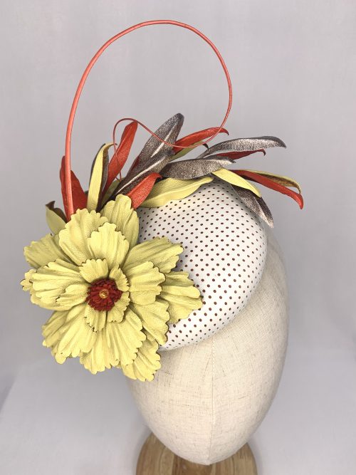 White perforated leather fascinator with large lemon leather flower trim, tri-colour leaves in red, gold and lemon, and a curled feather quill.