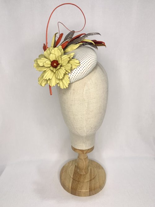 White perforated leather fascinator with large lemon leather flower trim, tri-colour leaves in red, gold and lemon, and a curled feather quill.