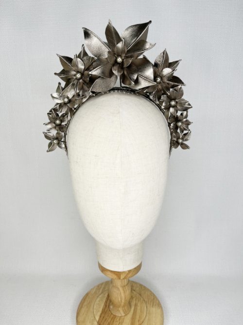 Front view of a calico mannequin wearing a pewter-coloured handmade leather flower headband in front of a light background.