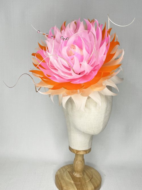 Large feather headpiece on a button base in pink, orange and apricot colours.