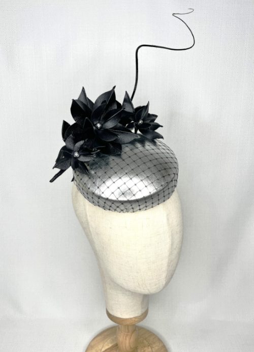 Silver leather button headpiece covered with black veiling, trimmed with black leather flowers and a curled quill.