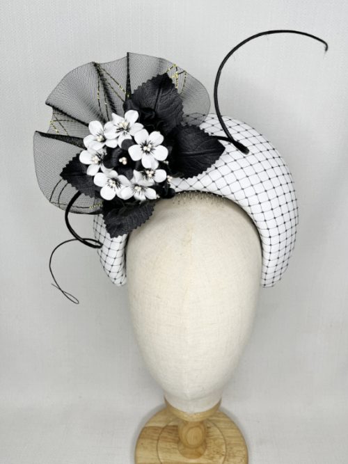 Black and white halo millinery trimmed with a bunch of flowers surrounded by leaves and crinoline.