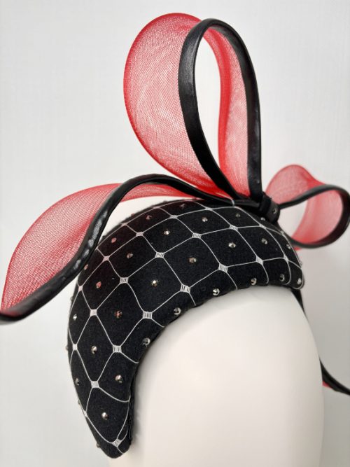 Close-up of a black felt fascinator with a red bow on a mannequin.