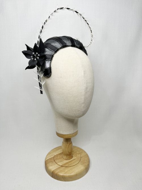 A mannequin wearing a black and silver fascinator with large curved quill.