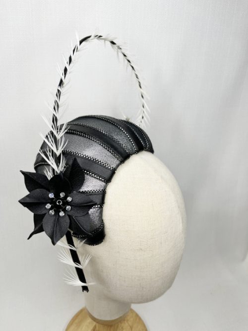 A mannequin wearing a black and silver fascinator with large curved quill.