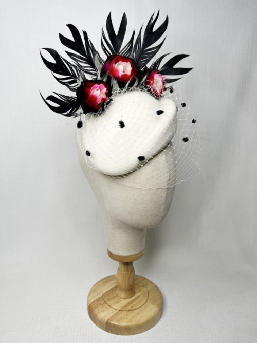 A mannequin wearing a light coloured felt fascinator with feathers and a spotted veil.