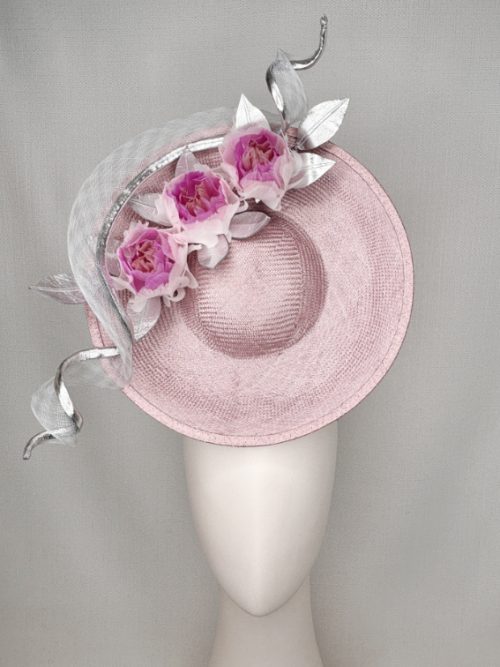 Mannequin head with no face wearing a large, front-facing hat with ombré pink-lilac feather flowers surrounded by a large crinoline swirl.