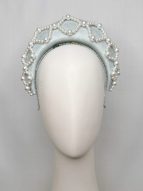 Mannequin head with no face wearing a pale blue fascinator headband with pearls.