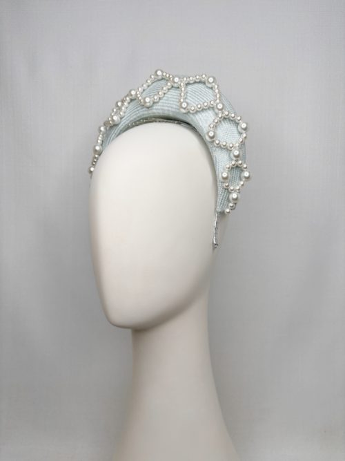 Mannequin head with no face wearing a pale blue fascinator headband with pearls.